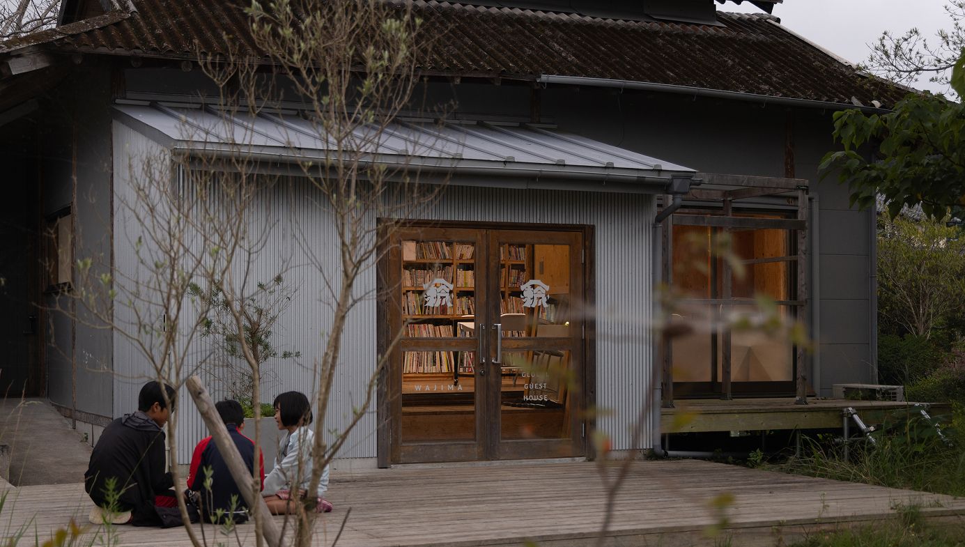 白い建物の前の木でできた床の上で子供達が座って話している